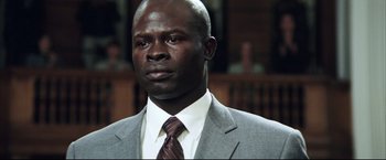 Movie still from “Blood Diamond” (2006), directed by Edward Zwick – A man in a suit and tie in a courtroom; Close Up shot, Low angle