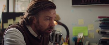 Movie still from “Booksmart” (2019), directed by Olivia Wilde – A man with long hair and a goatee is talking into a microphone; Close Up shot, Low angle
