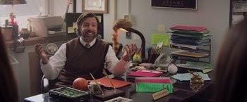 Movie still from “Booksmart” (2019), directed by Olivia Wilde – A man sitting at a desk in front of papers; Medium shot, Over the shoulder angle