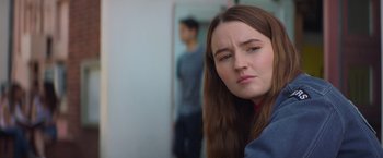 Movie still from “Booksmart” (2019), directed by Olivia Wilde – A young woman with long brown hair looking at the camera; Close Up shot, Over the shoulder angle