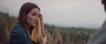 Movie still from “Booksmart” (2019), directed by Olivia Wilde – A woman holding an instrument up to her face; Close Up shot, Over the shoulder angle