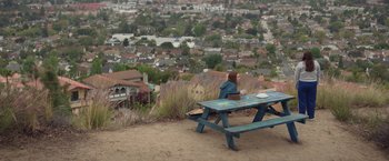 Movie still from “Booksmart” (2019), directed by Olivia Wilde – A woman sitting at a picnic table looking out over a city; Extreme Wide shot, High angle