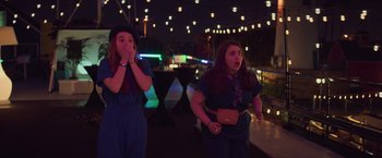 Movie still from “Booksmart” (2019), directed by Olivia Wilde – Two young women standing next to each other on a patio at night; Medium shot, Over the shoulder angle