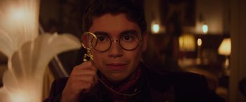 Movie still from “Booksmart” (2019), directed by Olivia Wilde – A young man wearing glasses holding a magnifying glass in front of his face; Close Up shot, Over the shoulder angle