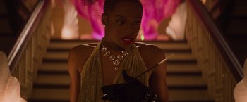 Movie still from “Booksmart” (2019), directed by Olivia Wilde – A woman in a gold dress holding a cigarette holder; Close Up shot, Over the shoulder angle