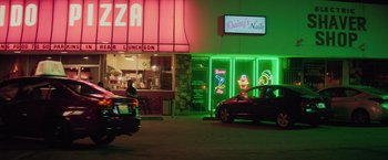 Movie still from “Booksmart” (2019), directed by Olivia Wilde – A car driving down a street past a building with neon lights on it; Extreme Wide shot, High angle