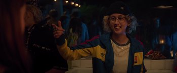 Movie still from “Booksmart” (2019), directed by Olivia Wilde – A woman in a hat and glasses is holding up a peace sign; Medium shot, Over the shoulder angle