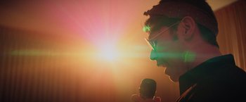 Movie still from “Booksmart” (2019), directed by Olivia Wilde – A man with glasses is holding a microphone; Close Up shot, Low angle