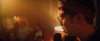 Movie still from “Booksmart” (2019), directed by Olivia Wilde – A person with glasses is speaking into a microphone; Extreme Close Up shot, Low angle