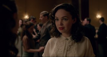 Movie still from “Brooklyn” (2015), directed by John Crowley – A woman in a white shirt is standing in front of a group of people; Close Up shot, Over the shoulder angle