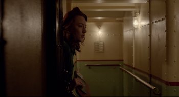 Movie still from “Brooklyn” (2015), directed by John Crowley – A woman leaning against a wall in a room; Medium shot, Low angle
