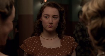 Movie still from “Brooklyn” (2015), directed by John Crowley – A woman with a polka dot dress and a pearl necklace; Close Up shot, Over the shoulder angle