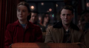 Movie still from “Brooklyn” (2015), directed by John Crowley – A man and a woman sitting in front of each other in front of a crowd; Medium shot, Over the shoulder angle