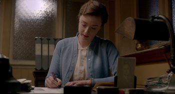Movie still from “Brooklyn” (2015), directed by John Crowley – A woman sitting at a table writing on a piece of paper; Medium shot, Over the shoulder angle