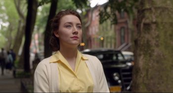 Movie still from “Brooklyn” (2015), directed by John Crowley – A woman in a yellow shirt and a white jacket; Close Up shot, Over the shoulder angle