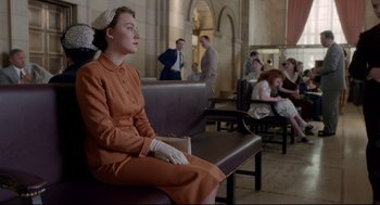 Movie still from “Brooklyn” (2015), directed by John Crowley – A woman sitting on top of a bench in a room; Wide shot, High angle
