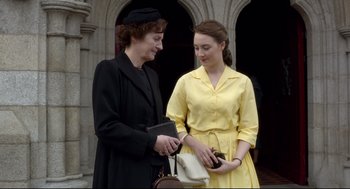 Movie still from “Brooklyn” (2015), directed by John Crowley – Two women standing next to each other holding purses; Medium shot, Over the shoulder angle