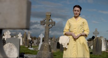 Movie still from “Brooklyn” (2015), directed by John Crowley – A woman in a yellow dress standing in front of a cross; Medium shot, Over the shoulder angle