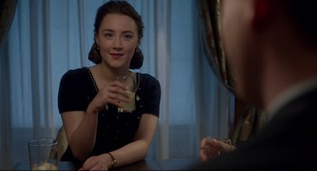 Movie still from “Brooklyn” (2015), directed by John Crowley – A woman sitting at a table holding a drink; Close Up shot, Over the shoulder angle