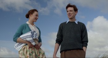 Movie still from “Brooklyn” (2015), directed by John Crowley – A man and a woman standing next to each other in front of a sky background; Medium shot, Low angle