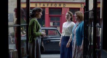 Movie still from “Brooklyn” (2015), directed by John Crowley – A group of women standing next to each other on the sidewalk; Medium shot, Over the shoulder angle