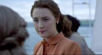 Movie still from “Brooklyn” (2015), directed by John Crowley – A young woman in an orange shirt is looking at the camera; Close Up shot, Over the shoulder angle