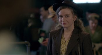 Movie still from “Brooklyn” (2015), directed by John Crowley – A woman wearing a hat standing in front of a crowd; Close Up shot, Over the shoulder angle