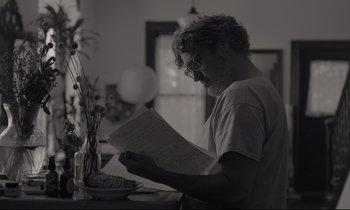 Movie still from “C'mon C'mon” (2021), directed by Mike Mills – A man sitting at a table reading a paper; Medium shot, Over the shoulder angle