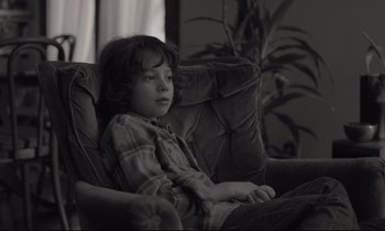 Movie still from “C'mon C'mon” (2021), directed by Mike Mills – A young boy sitting in a chair in a living room; Medium shot, High angle