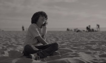 Movie still from “C'mon C'mon” (2021), directed by Mike Mills – A boy sitting on the sand on the beach; Medium shot, Low angle