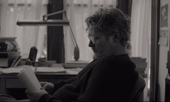 Movie still from “C'mon C'mon” (2021), directed by Mike Mills – A black and white photo of a man reading a paper; Close Up shot, Over the shoulder angle