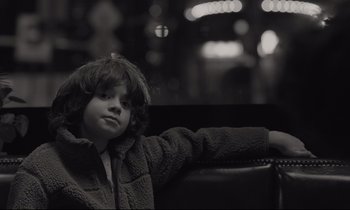 Movie still from “C'mon C'mon” (2021), directed by Mike Mills – A young boy sitting on a chair in a room; Close Up shot, Over the shoulder angle