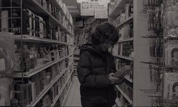 Movie still from “C'mon C'mon” (2021), directed by Mike Mills – A young boy is looking at a book in a store aisle; Medium shot, Over the shoulder angle
