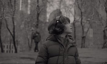 Movie still from “C'mon C'mon” (2021), directed by Mike Mills – A young boy wearing headphones while standing in a wooded area; Medium shot, Over the shoulder angle