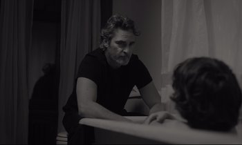 Movie still from “C'mon C'mon” (2021), directed by Mike Mills – A black and white photo of a man sitting at a table; Medium shot, Over the shoulder angle