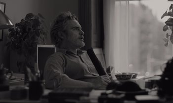 Movie still from “C'mon C'mon” (2021), directed by Mike Mills – Black and white photograph of a man sitting at a table; Medium shot, Over the shoulder angle