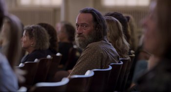 Movie still from “CODA” (2021), directed by Sian Heder – A man with a beard is sitting in a row of chairs; Close Up shot, Over the shoulder angle