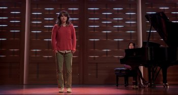 A woman standing on a stage next to a piano