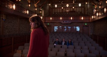 Movie still from “CODA” (2021), directed by Sian Heder – A woman standing in front of a group of people in an auditorium; Wide shot, Over the shoulder angle
