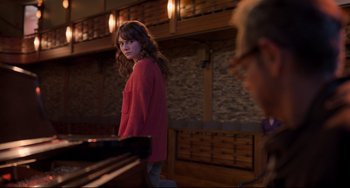 Movie still from “CODA” (2021), directed by Sian Heder – A woman standing next to a piano in a darkened room; Medium shot, Over the shoulder angle