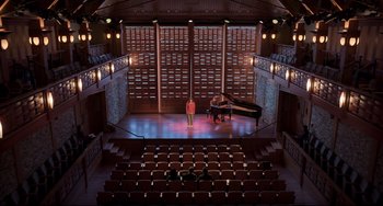 Movie still from “CODA” (2021), directed by Sian Heder – A man standing in front of a grand piano in an auditorium; Extreme Wide shot, High angle