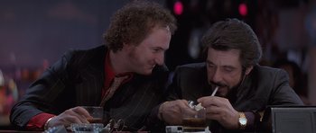 Movie still from “Carlito's Way” (1993), directed by Brian De Palma – Two men sitting at a dinner table and one of the men is smoking a cigarette; Close Up shot, Low angle