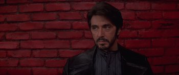 Movie still from “Carlito's Way” (1993), directed by Brian De Palma – A person wearing a black jacket near a brick wall; Close Up shot, Over the shoulder angle