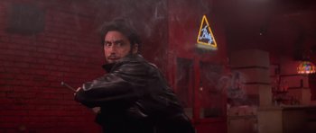 Movie still from “Carlito's Way” (1993), directed by Brian De Palma – A man in a leather jacket is smoking a cigarette in front of a building; Medium shot, Low angle
