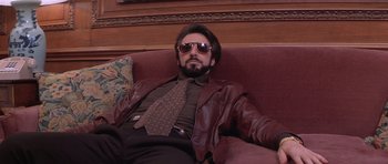 Movie still from “Carlito's Way” (1993), directed by Brian De Palma – A man in a suit and tie sitting on a couch; Medium shot, Low angle