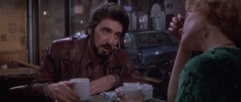Movie still from “Carlito's Way” (1993), directed by Brian De Palma – A man sitting at a table holding a cup of coffee; Close Up shot, Over the shoulder angle