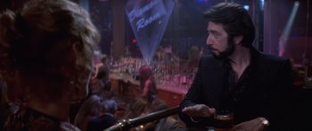 Movie still from “Carlito's Way” (1993), directed by Brian De Palma – A man sitting at a bar in front of a bunch of people; Close Up shot, Over the shoulder angle
