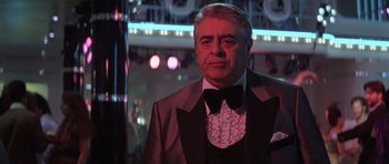 Movie still from “Carlito's Way” (1993), directed by Brian De Palma – An older man wearing a suit and bow tie in front of lights; Close Up shot, Over the shoulder angle