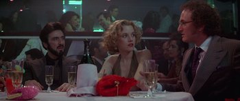Movie still from “Carlito's Way” (1993), directed by Brian De Palma – A woman sitting at a table with a glass of wine; Medium shot, Low angle