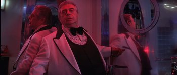 Movie still from “Carlito's Way” (1993), directed by Brian De Palma – A man in a suit and bow - tie holding a remote control; Medium shot, Low angle